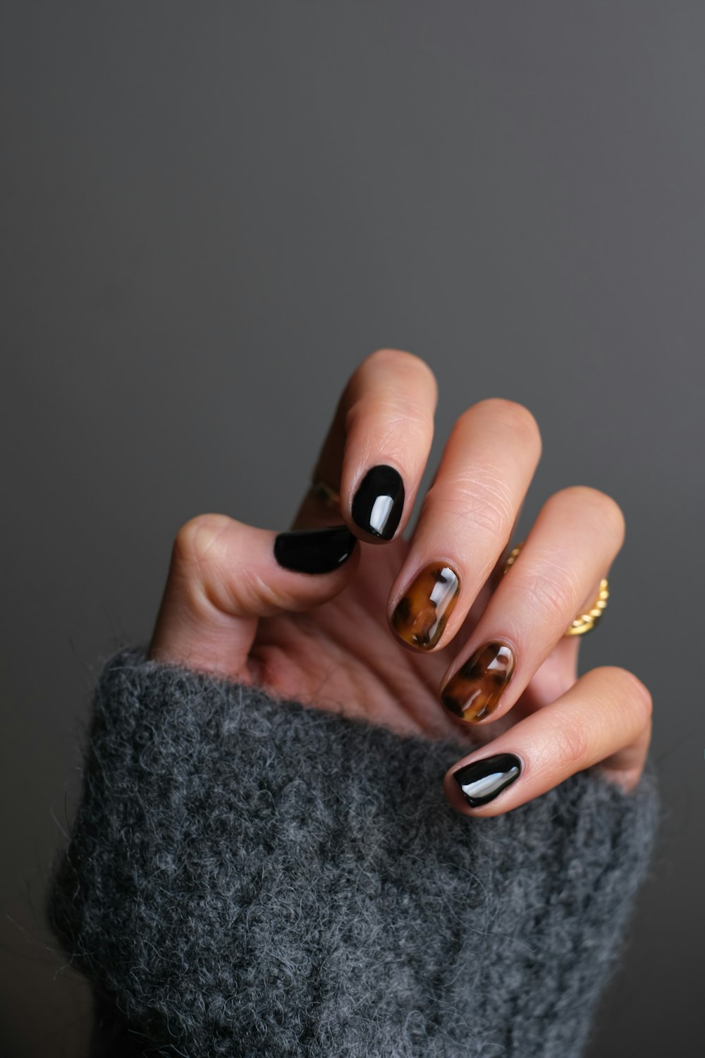 Near-black nails with a gold accent finger, hand tucked into a grey sleeve