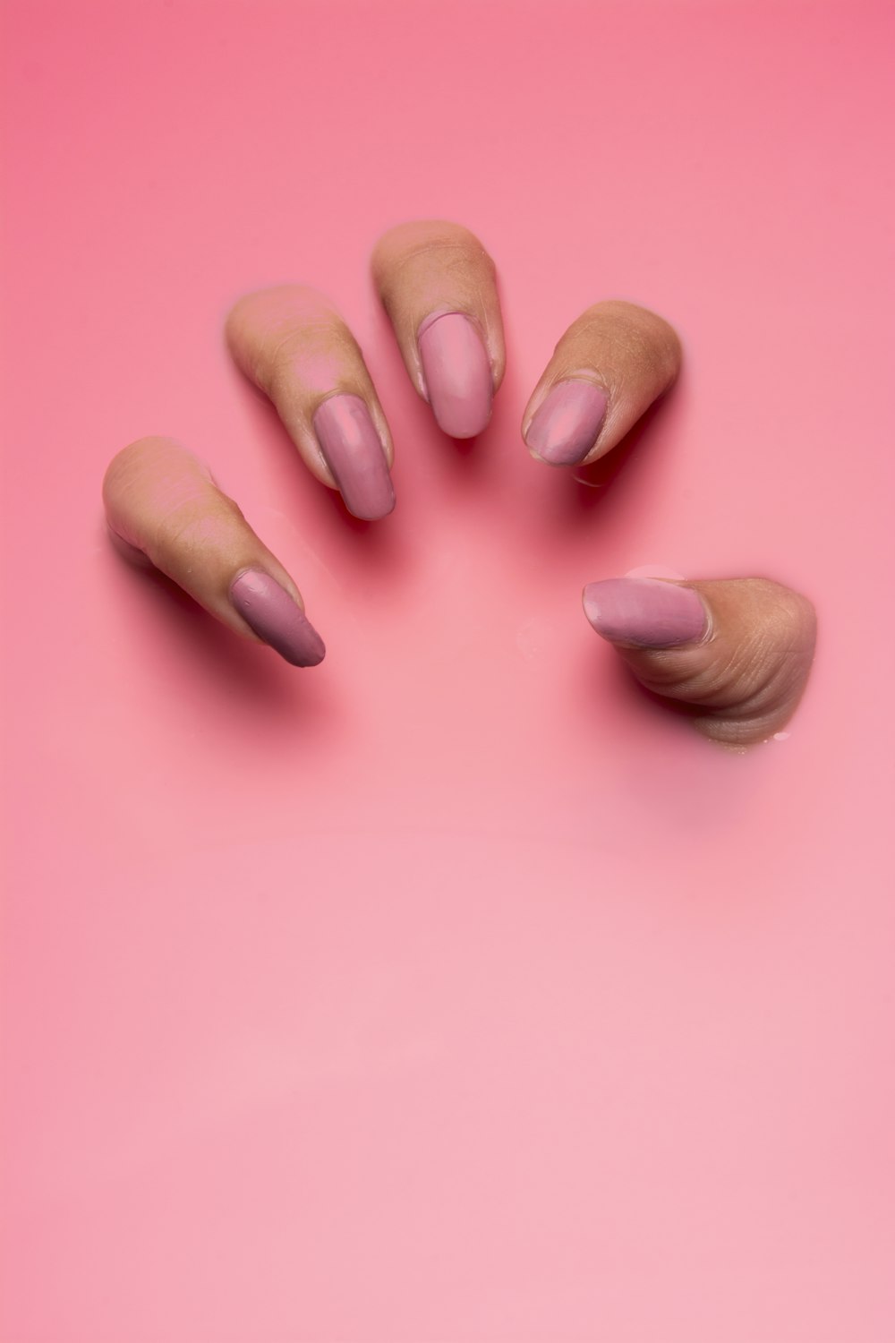 Mauve nails photographed against a soft pink background